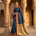 Woman in a traditional blue saree with gold patterns standing in an architectural setting.