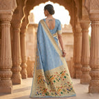 Woman in a blue saree with floral patterns standing in an architectural setting.