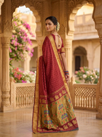 Woman in a traditional red and gold saree standing in an ornate architectural setting with floral decorations.