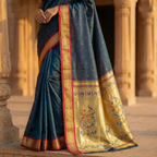 Blue saree with gold border and intricate design held by a person in an outdoor setting.