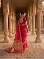 Woman in a pink saree standing in an architectural setting with columns.