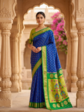 Woman in a blue and green saree standing in an ornate architectural setting.