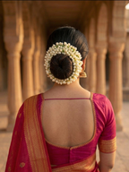 Woman in a red saree with a floral hairpiece standing in an architectural setting.