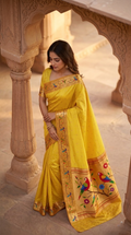 Woman in a yellow saree with intricate designs standing in an architectural setting.