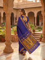 Woman in a blue saree with gold patterns standing in an outdoor courtyard.