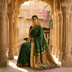Woman in a green saree with gold details sitting in an ornate architectural setting.