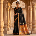 Woman in a traditional black and gold saree standing in an architectural setting.