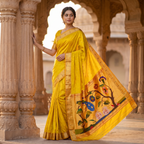 Woman in a yellow saree with floral patterns standing in an architectural setting.