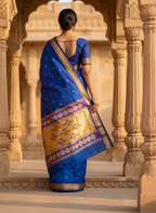 Woman in a blue saree with gold patterns standing in an architectural setting.