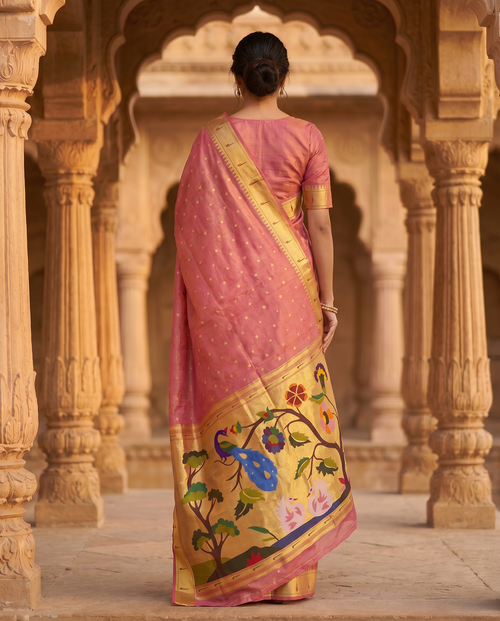 Woman in a pink saree with a floral border standing in an architectural setting.