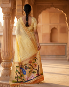 Woman in a traditional yellow saree with floral patterns standing in an architectural setting.